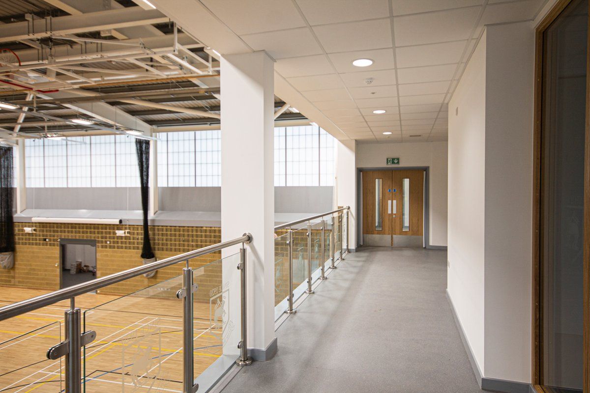 Bright first-floor corridor overlooking a sports hall through a glass balustrade